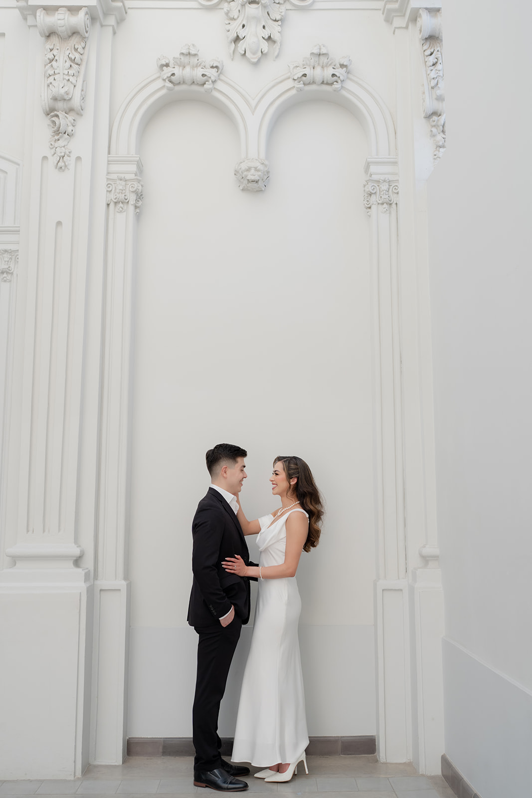 Full length portrait of Kelsey Margarita and José Elías beneath ornate white arches